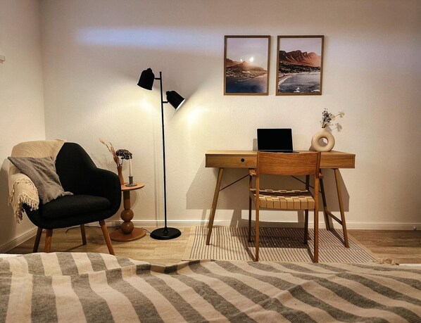 Una habitación con escritorio, silla, lámpara y dos cuadros en la pared.