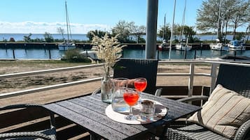 A table with a drink, a glass, and a vase with flowers, overlooking a marina with boats.