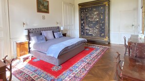 A bedroom with a large bed, a red and blue patterned rug, a wooden desk, and a large ornate cabinet. - Countryside Castle With Concierge Luxury (Maigné)