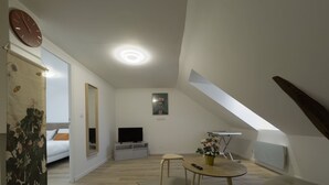 A modern, well-lit room with a bed, a TV, a small table with a vase, and a painting on the wall. - Modern Comfort in the Heart of Le Mans (Le Mans)