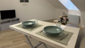 A modern dining area with a table set for two, a television in the background, and a framed picture on the wall. - Modern Comfort in the Heart of Le Mans (Le Mans)