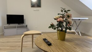 A modern living room with a round wooden table, a remote control, a potted plant, a television, and a small white cabinet. - Modern Comfort in the Heart of Le Mans (Le Mans)