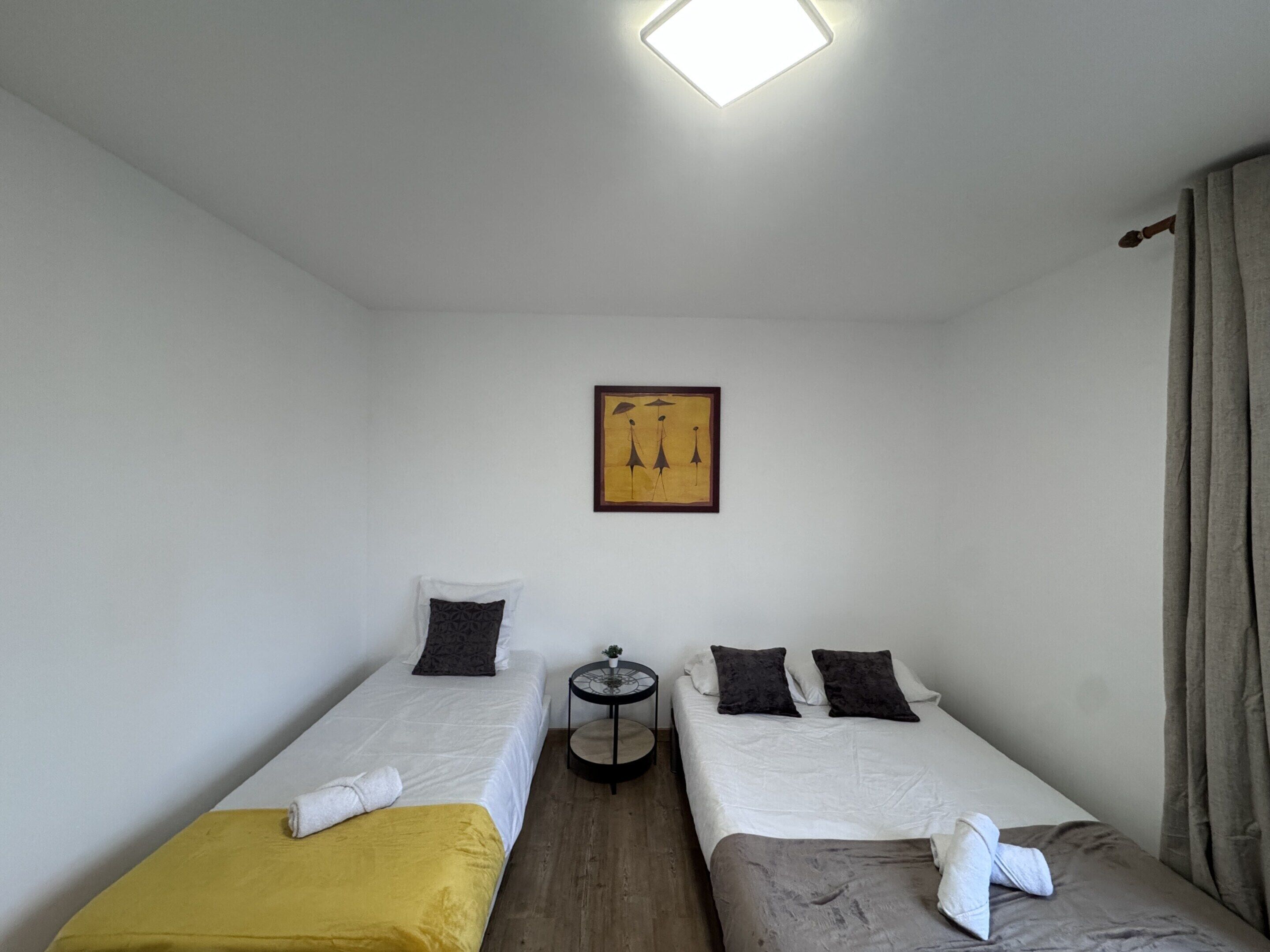 Una stanza piccola e pulita con due letti singoli, un tavolino e un quadro appeso al muro.