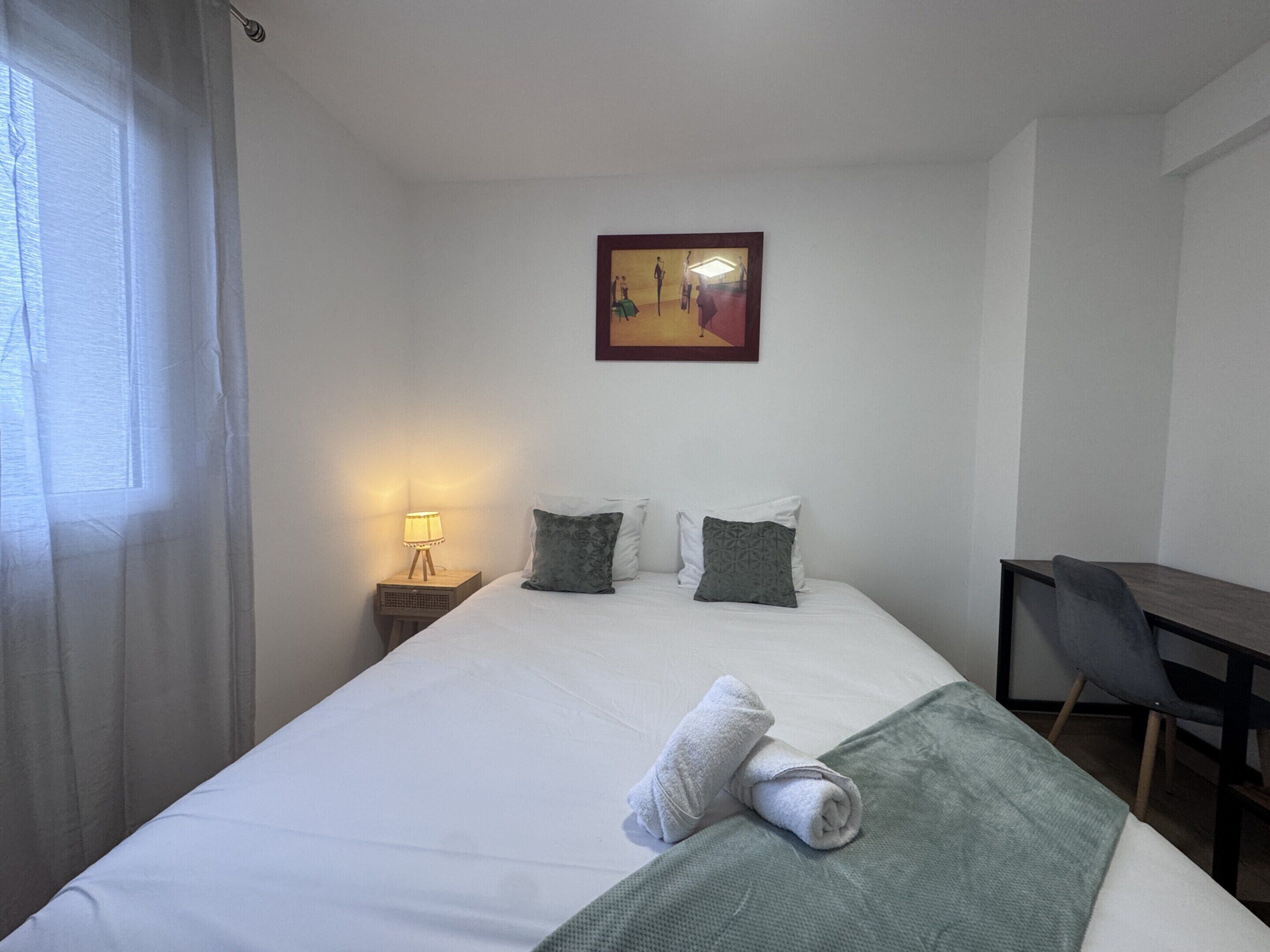 Une chambre d’hôtel avec un lit, un bureau, une chaise, une lampe et un tableau au mur.