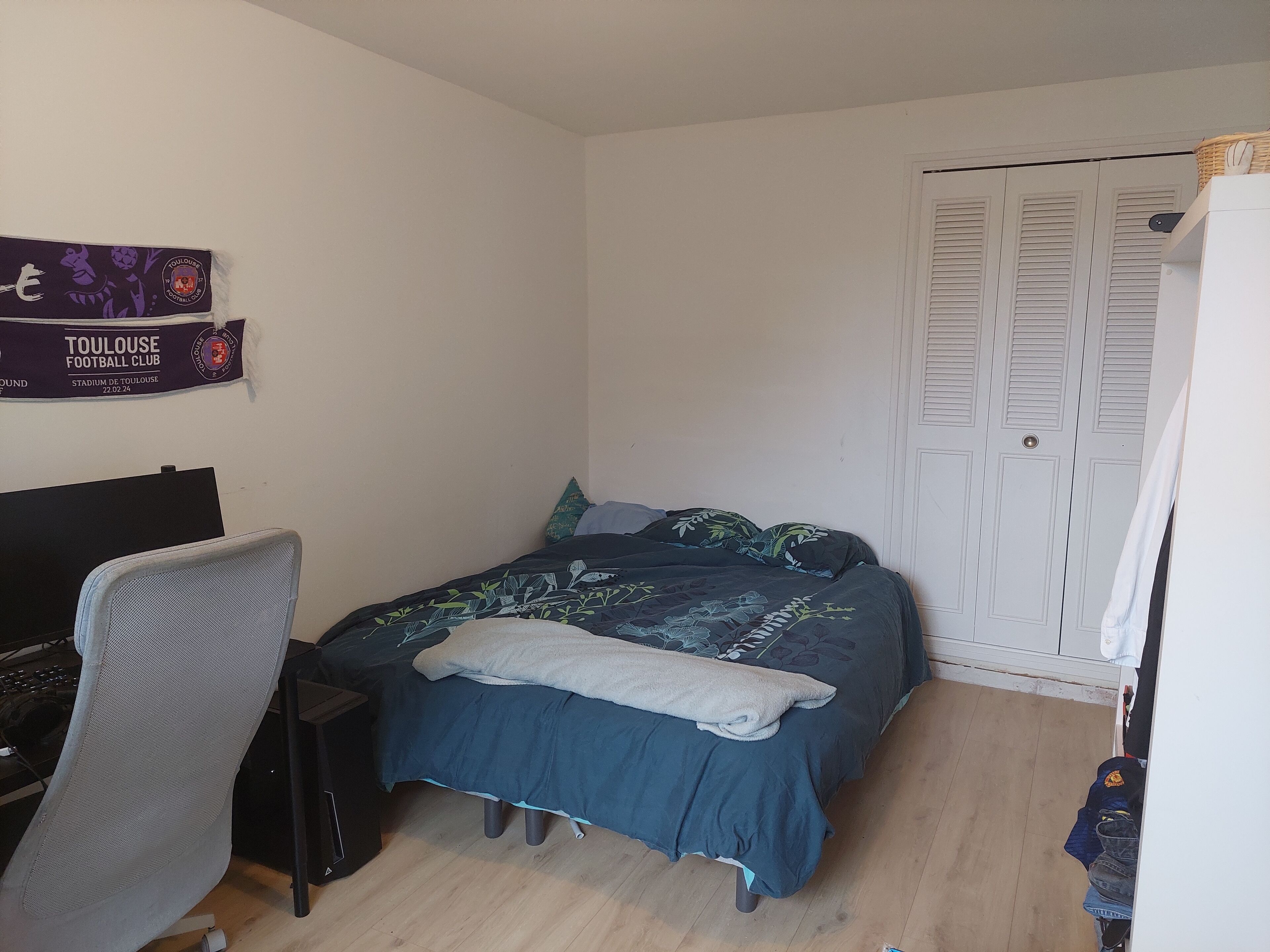 A bedroom with a bed, a desk, and a chair. There is a closet with white doors and a sign on the wall.