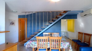 A dining area with a staircase, wooden chairs, and a table with a floral tablecloth. - Apartment in Spain Near Sandy Beach (Torroella de Montgrí)