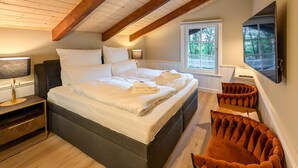 A bedroom with a large bed, two bedside lamps, a wooden ceiling, and a window with a view of trees.
