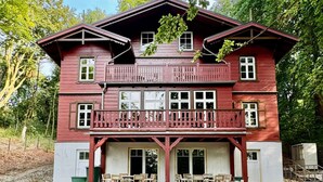 A two-story wooden house with a balcony, a covered porch, and a small attached structure.