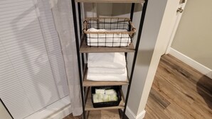 A wooden shelf unit with a potted plant, a woven basket, and a black basket with white towels. - Charming 3-bedroom house with AC, WiFi in fabulous Mobile (Mobile)