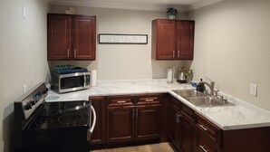 A kitchen with wooden cabinets, a microwave, stove, sink, and a framed sign on the wall. - Charming 3-bedroom house with AC, WiFi in fabulous Mobile (Mobile)