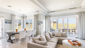 A spacious living area with a large beige sectional sofa, a dining table with chairs, and a glass coffee table.