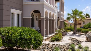 A multi-story hotel with a symmetrical facade, arched windows, and a landscaped garden with palm trees and shrubs.