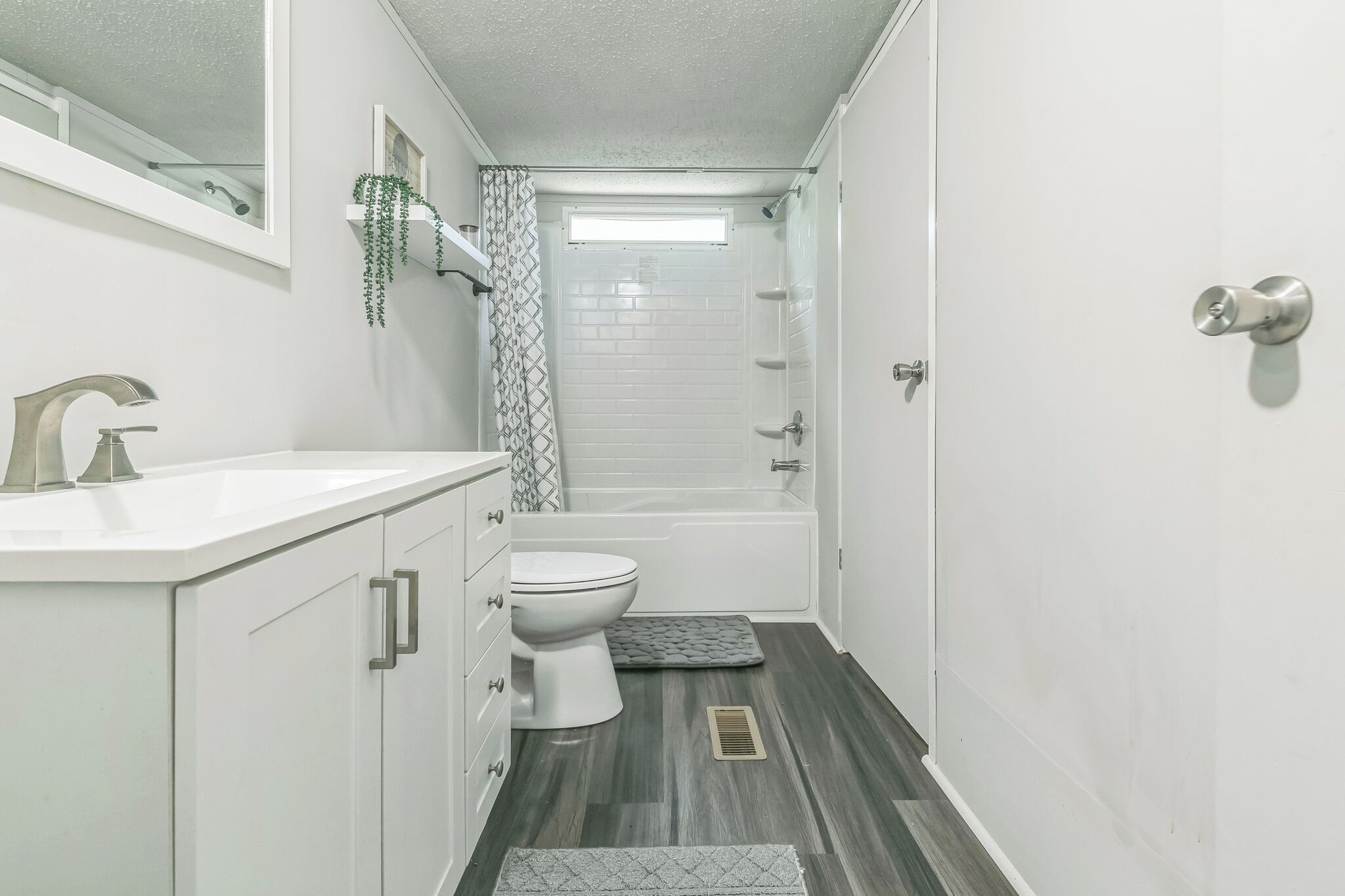 Ein schmales Badezimmer mit einem weißen Waschbecken, WC und Dusche.