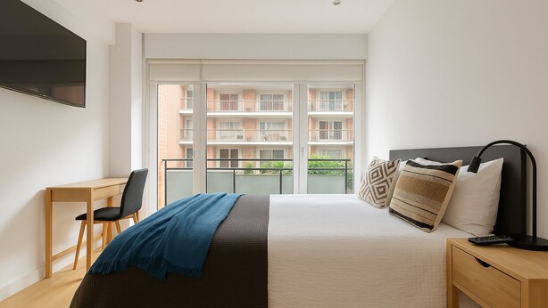 A bedroom with a bed, a desk, a chair, a TV, and a balcony with a view of other buildings. - Spacious apartment in the city center (Bilbao)