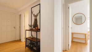 A hallway with wooden flooring, a white door, a framed deer head artwork, a small table with potted plants, and a round mirror on the wall. - Spacious apartment in the city center (Bilbao)