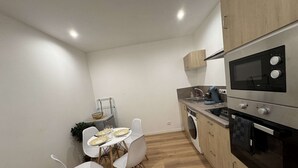 Une cuisine compacte équipée d’un four à micro-ondes, d’un four et d’un lave-linge. On y trouve une table à manger avec des chaises et une petite plante.