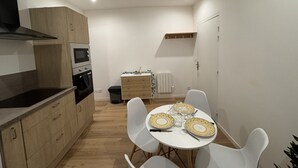 Une cuisine compacte dotée d’appareils électroménagers modernes, un coin repas avec des chaises blanches et une table dressée pour deux personnes, ainsi qu’un petit meuble contenant un four à micro-ondes.