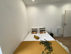 A neatly made bed with a yellow blanket, two pillows with striped patterns, and a small bedside table with a lamp.