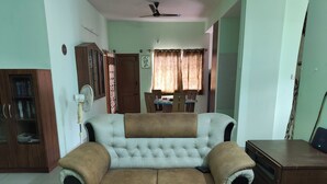 A living room with a sofa, a wooden cabinet, a fan, and a dining area in the background. - Charming & Spacious 2-bedroom apartment in amazing Bengaluru with WiFi, fitness. (Bengaluru)
