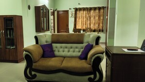 A living room with a brown sofa, a wooden cabinet, and a desk with a laptop. - Charming & Spacious 2-bedroom apartment in amazing Bengaluru with WiFi, fitness. (Bengaluru)