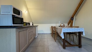 Une cuisine équipée d’un four à micro-ondes, d’un évier et de meubles de rangement en bois. On y trouve une table à manger avec des chaises, ainsi qu’une horloge au mur.