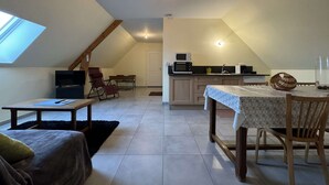Une chambre confortable située sous les toits, avec un puits de lumière, une petite kitchenette et un coin repas comprenant une table et des chaises.