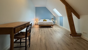 Une chambre aménagée dans les combles, avec un plafond en pente, un bureau en bois, un lit et une lucarne.