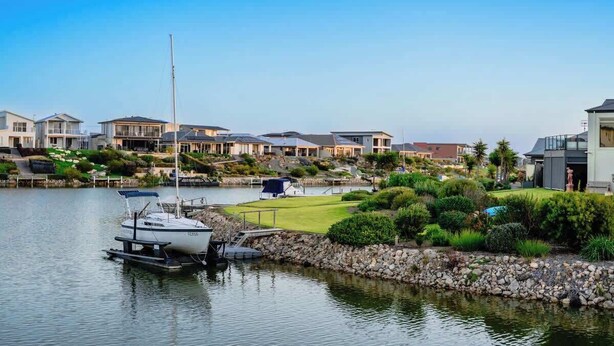 A marina with boats docked, surrounded by residential buildings with a well-maintained lawn and a clear sky. - Waterfront house private jetty kayaks provided (Hindmarsh Island)