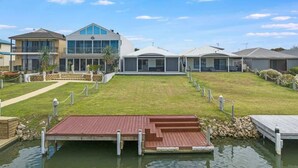 A waterfront property with a grassy lawn, a wooden dock, and modern buildings with large windows and balconies. - Waterfront house private jetty kayaks provided (Hindmarsh Island)