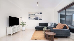 A modern living room with a flat-screen TV, a grey sofa, a coffee table, and a large window. - Waterfront house private jetty kayaks provided (Hindmarsh Island)