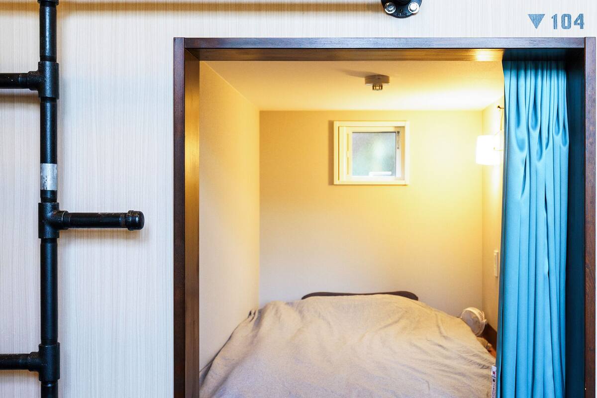 Ett hotellrum med en säng, ett fönster med en fotoram och en dörr med ett nummerskylt.