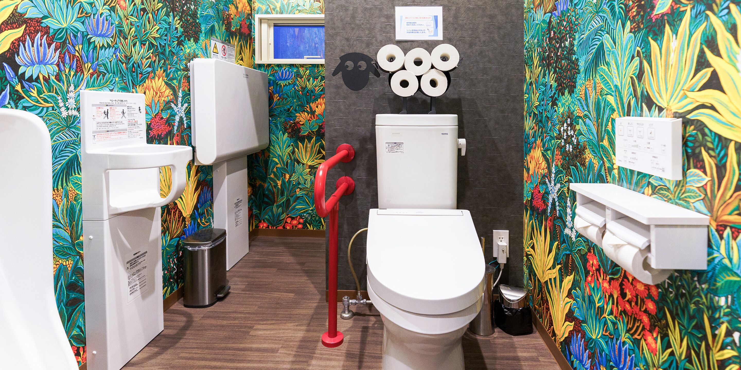 A bathroom with a colorful floral wallpaper, a white toilet, a bidet, and a trash bin.