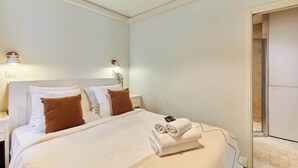 A hotel room with a neatly made bed, a nightstand with a lamp, and a bathroom visible through an open door. - Apartement With AC Center of Paris (Paris)