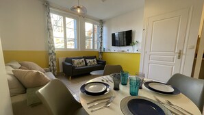 Un comedor con una mesa redonda dispuesta para cuatro personas, un sofá y un televisor montado en la pared.