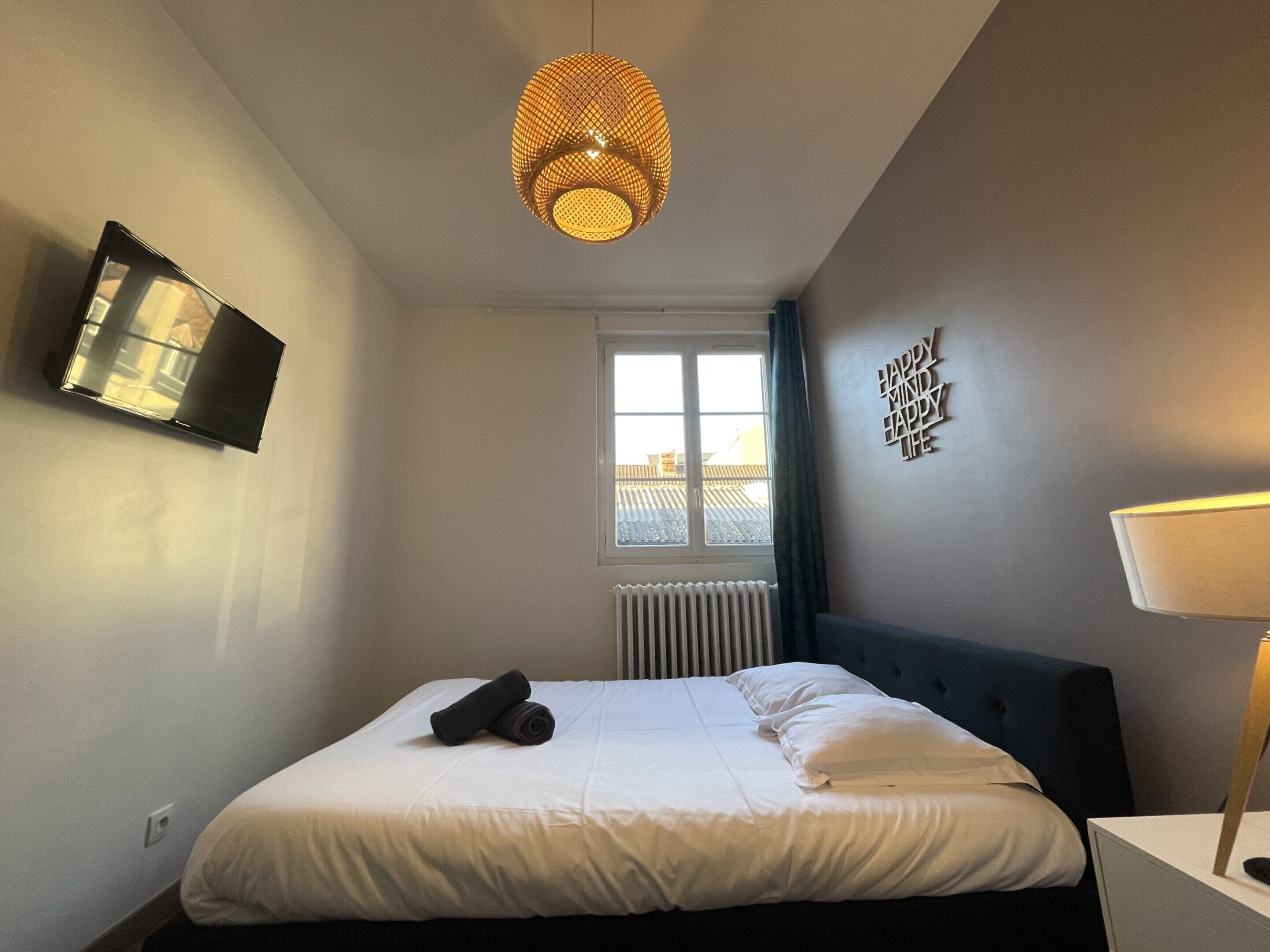 Une chambre d’hôtel avec un lit, un téléviseur fixé au mur, une fenêtre avec des rideaux et un élément décoratif mural.