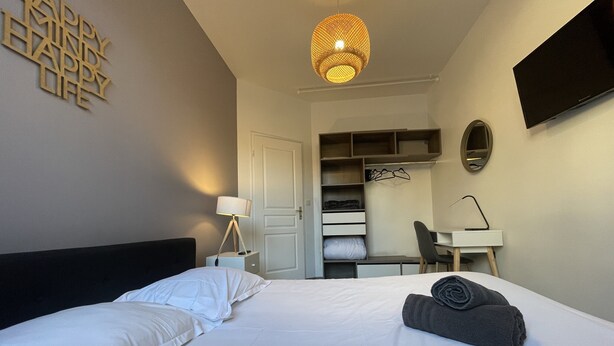 Una habitación de hotel con cama, escritorio, silla, armario y televisor.