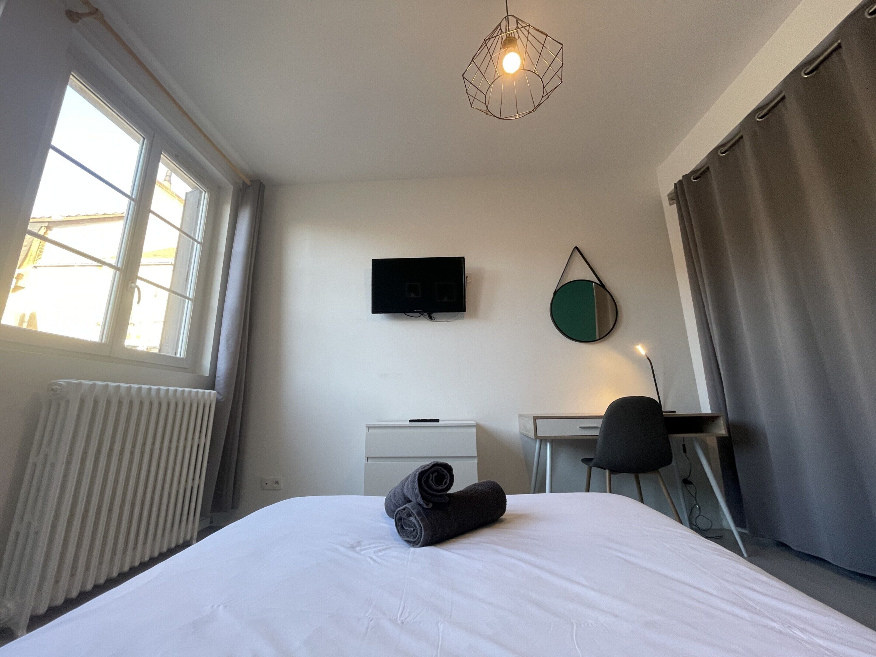 A hotel room with a bed, a desk, a chair, a TV, and a window with curtains.
