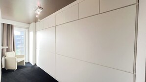 Habitación de hotel con una pared grande de paneles blancos, una alfombra negra, un sillón blanco y una pequeña mesa.
