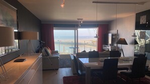 Una sala de estar moderna con un ventanal grande, comedor y kitchenette.