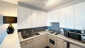 Una cocina compacta con armarios blancos, estufa, microondas y pileta.