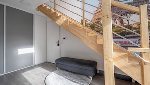 Un escalier moderne avec des finitions en bois et une rampe en verre, menant à une pièce offrant une vue sur la Tour Eiffel.