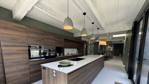 Et moderne køkken med en stor ø, mørke træskabe, rustfrie stål hvidevarer og hængende lamper.