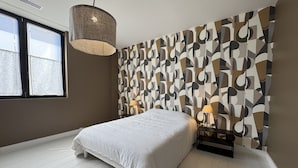 Et soveværelse med en stor seng, en hængende lampe, et natbord med lampe, og en væg med mønster.
