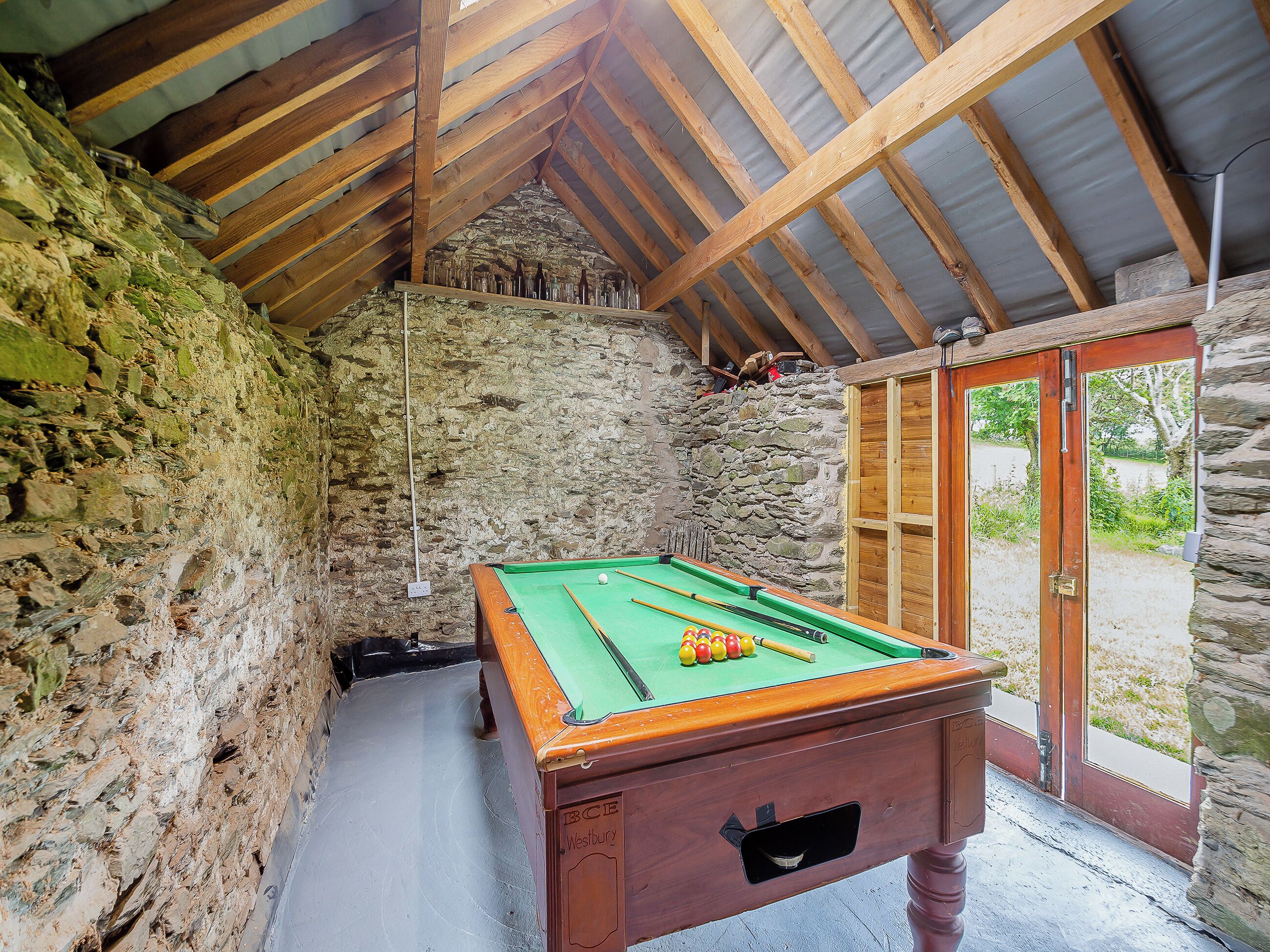 A pool table in a rustic room with stone walls and wooden beams.