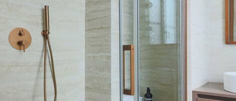 A modern bathroom with a glass-enclosed shower, a wooden vanity, and a marble-tiled wall.
