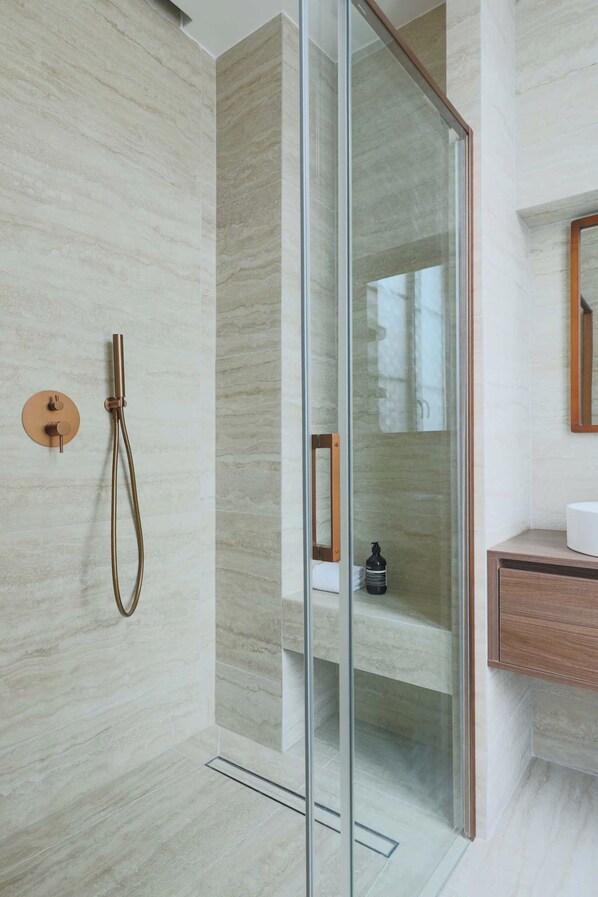 Un baño moderno con ducha de vidrio, tocador de madera y pared de azulejos de mármol.