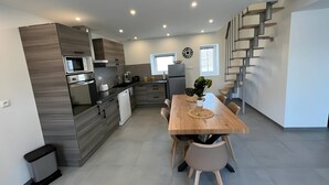 Eine moderne Küche mit integrierten Geräten, ein Essbereich mit Holztisch und Stühlen sowie eine minimalistisch gestaltete Treppe.