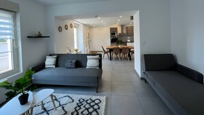 Ein modernes Wohnzimmer mit grauem Sofa, einem Essbereich mit Holztisch und Stühlen sowie einer Küche im Hintergrund.
