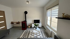 Ein modernes Wohnzimmer mit Sofa, Couchtisch, Fernseher, Kamin und einem Fenster mit Jalousien.