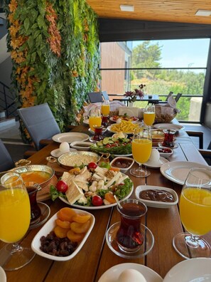 A breakfast buffet with various dishes, drinks, and a view of greenery outside. - Helios Kaz Dağları 2.BLOK (Edremit)